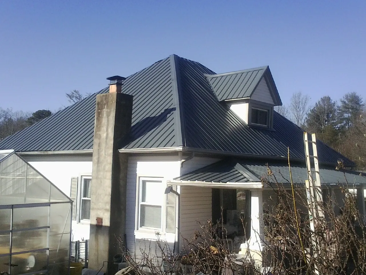 Dark blue standing seam metal roof on a white farmhouse with dormer — Slate & Tile Roof Repair by Roofing Brothers in Casey