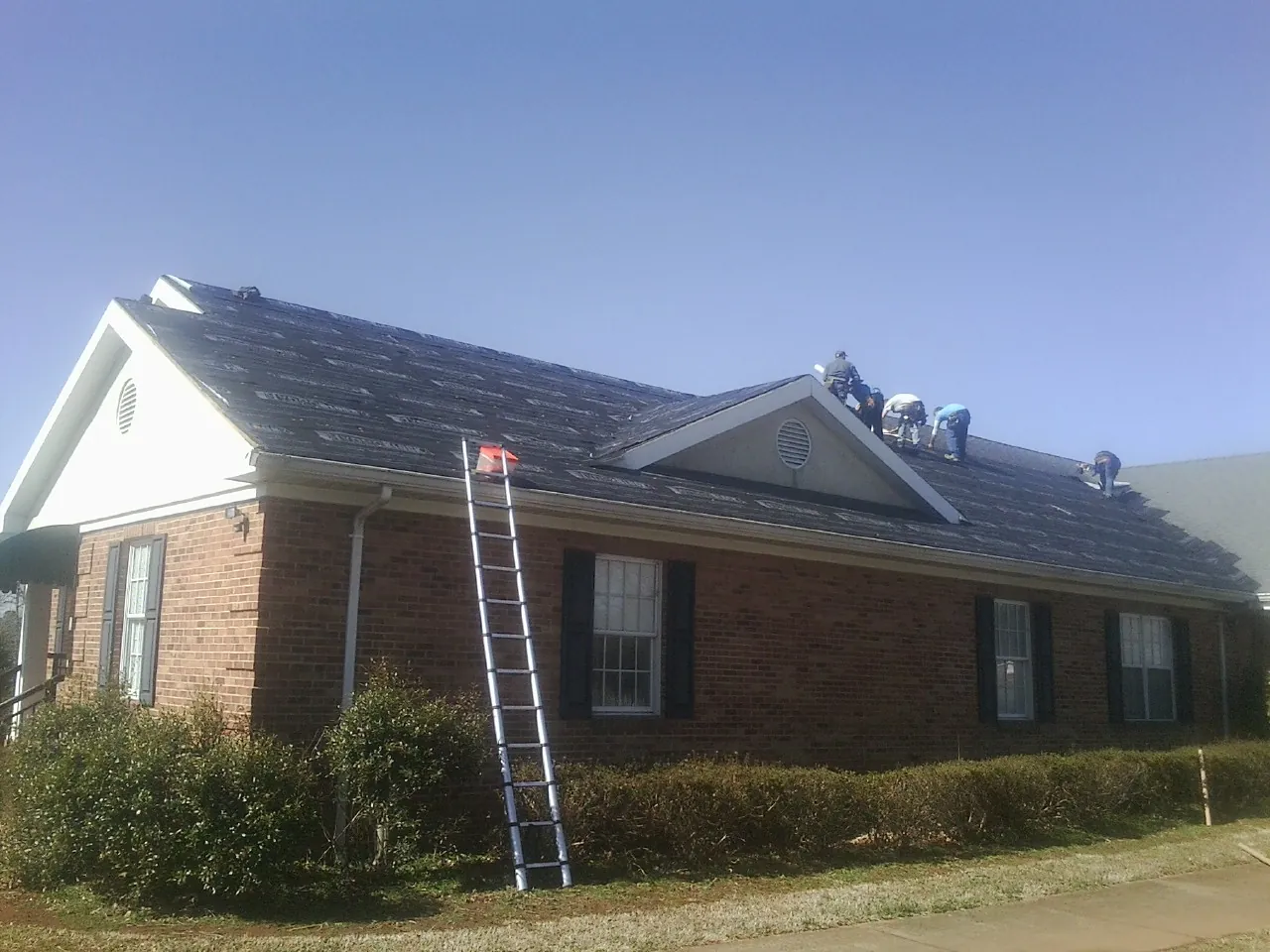 Crew tearing shingles off a brick ranch roof with a ladder set — Metal Roof Repair work by our crew in Casey