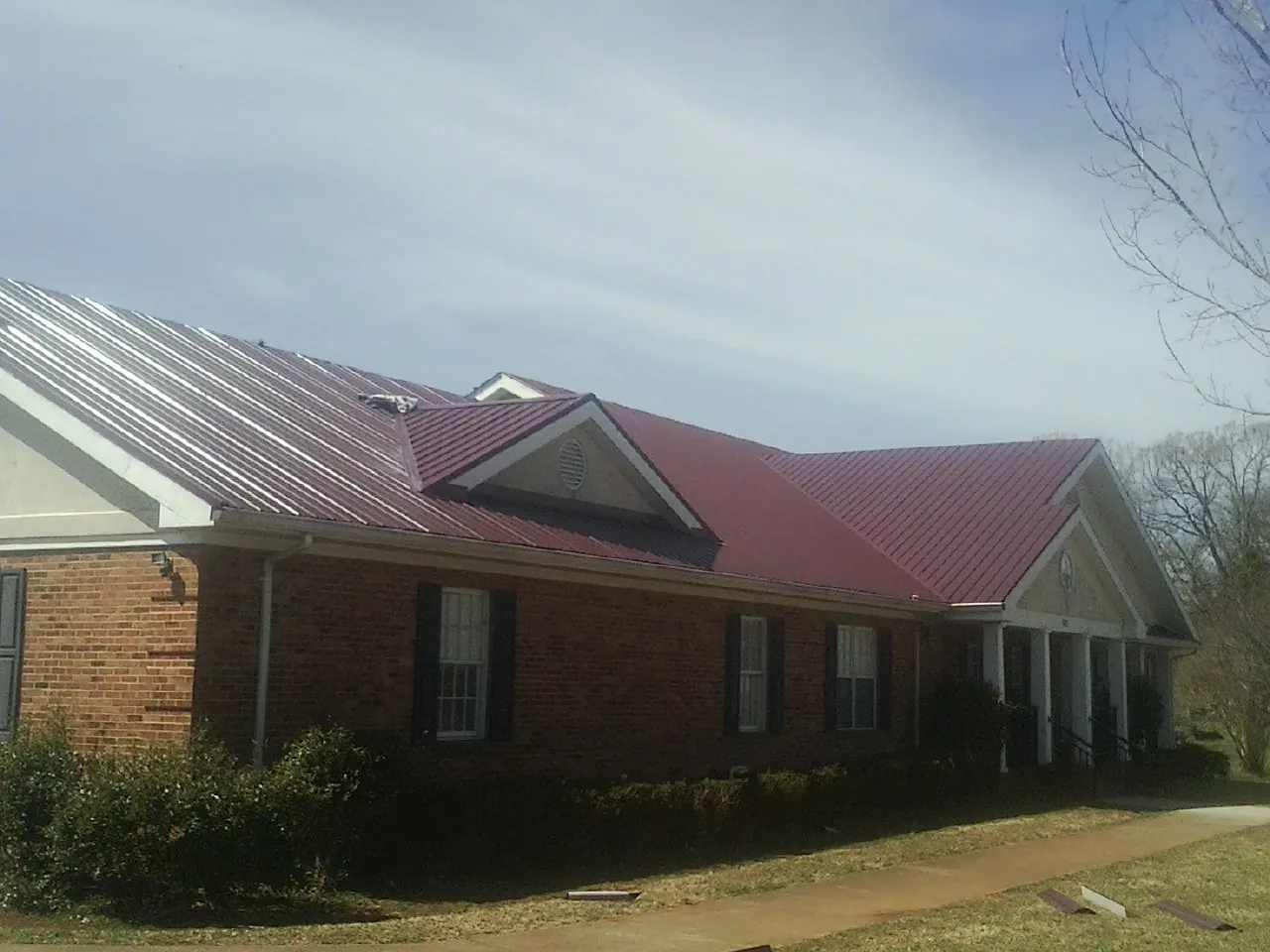 Red metal roof with gabled entries on a long brick building, from a Hail Damage Roof Repair job in Casey
