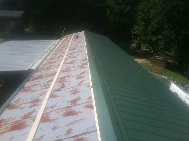 Old rusted panels beside newly installed green metal roofing — Wind Damage Roof Repair by Roofing Brothers in Casey