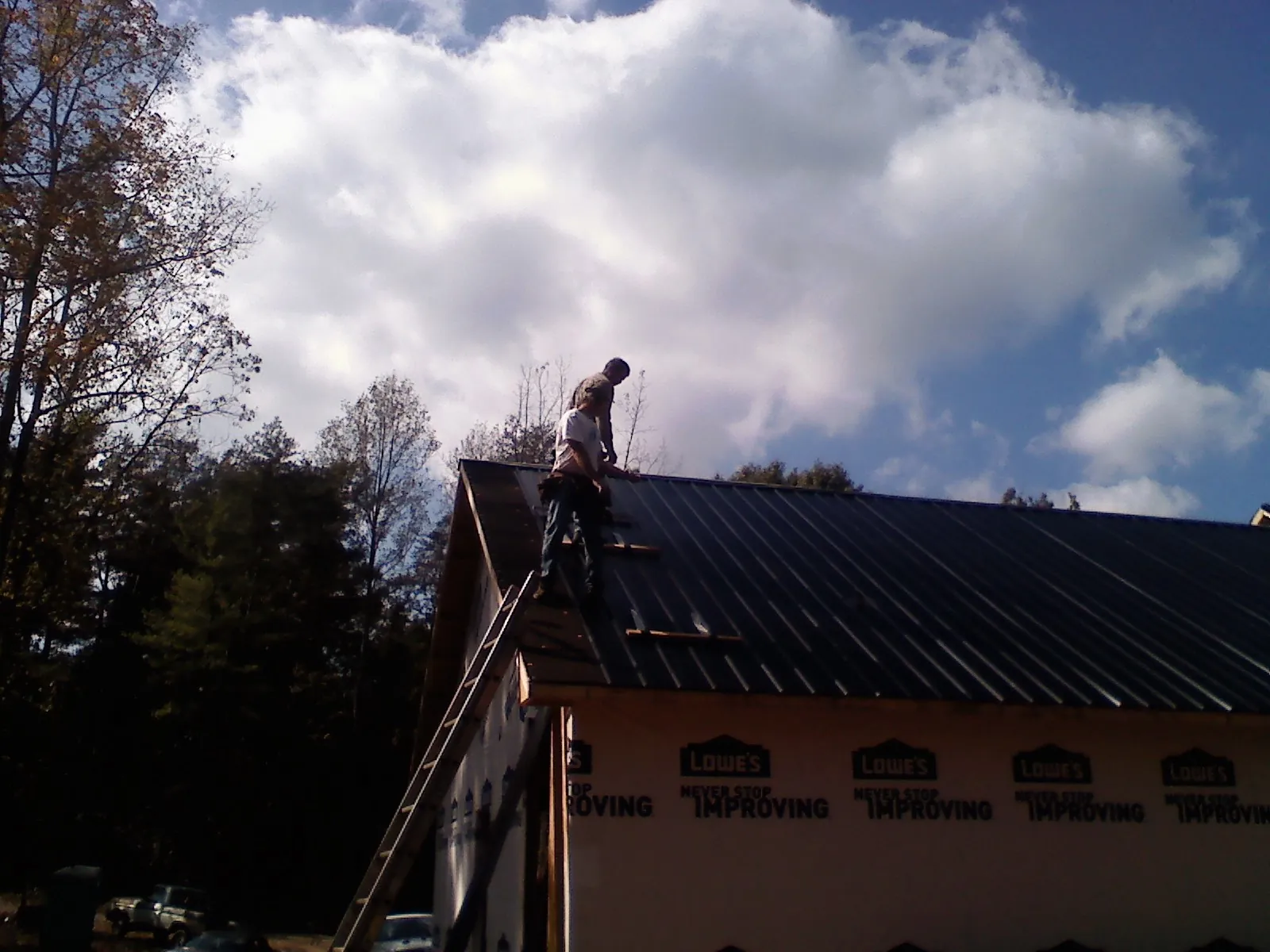 Roofer fastening dark metal panels high against a cloudy sky, from a Roof Inspection job in Casey