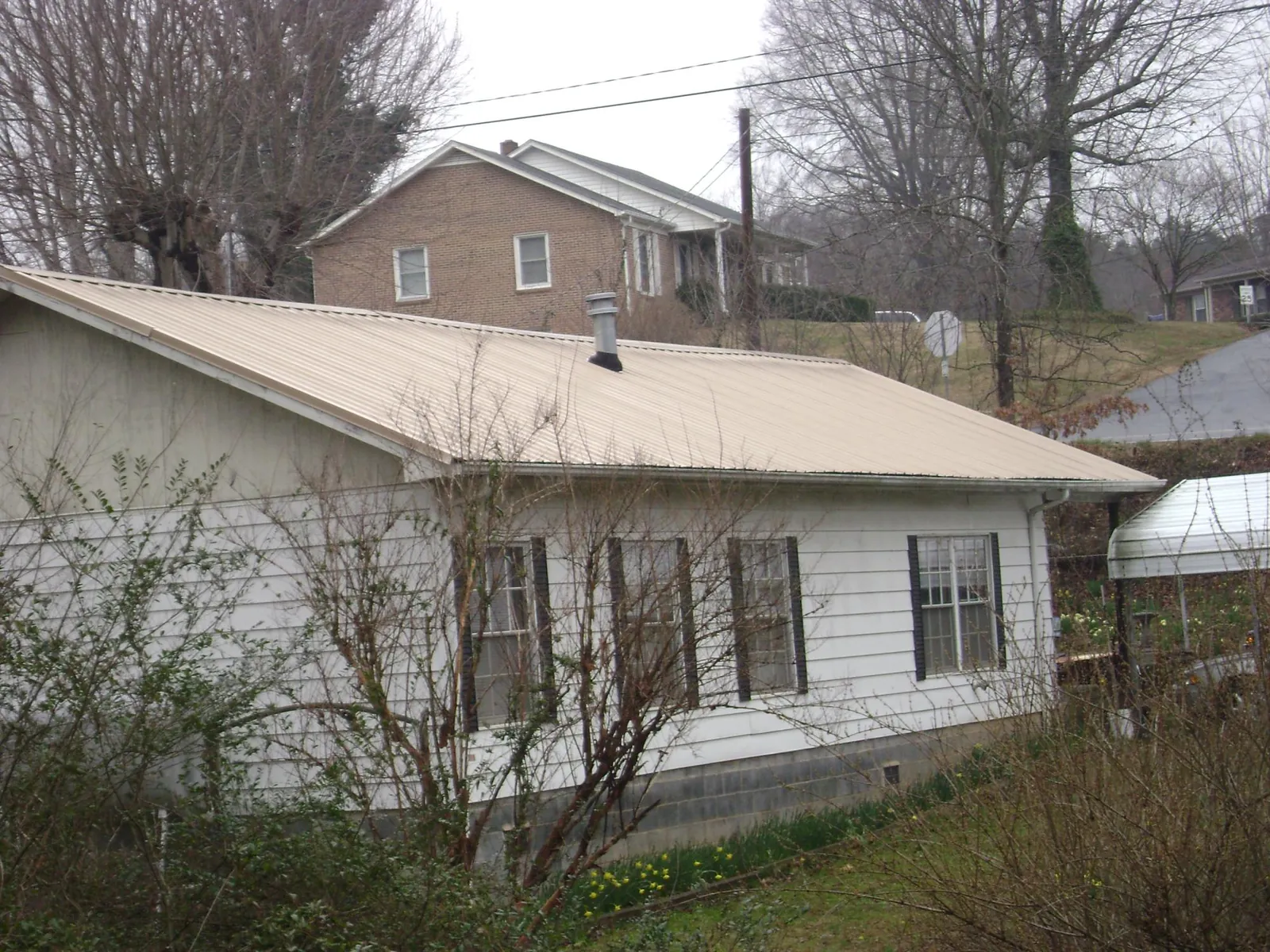 Tan metal roof on a white sided house set into a hillside — Commercial Roofing by Roofing Brothers in Casey